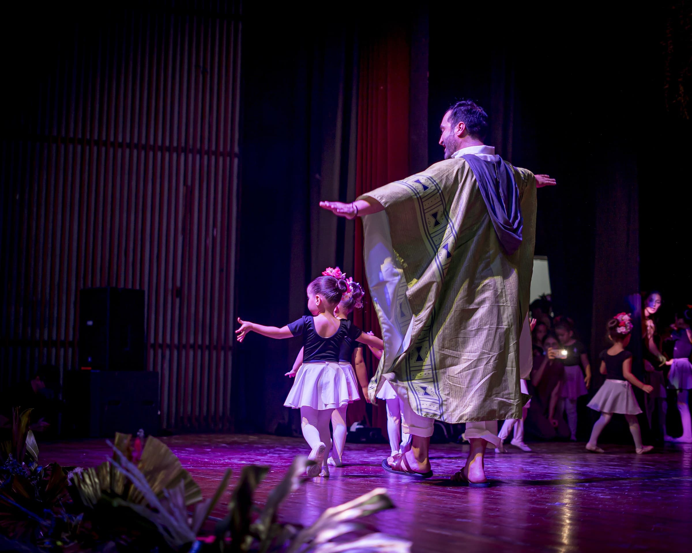 Personaje con poncho y niñas bailarinas en escena
